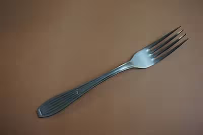 Silver metal fork with four prongs on a brown background